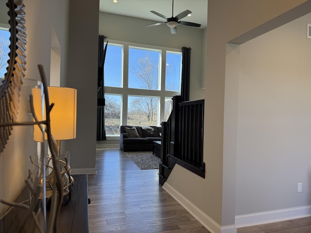 interior space with baseboards, wood finished floors, a towering ceiling, and a ceiling fan