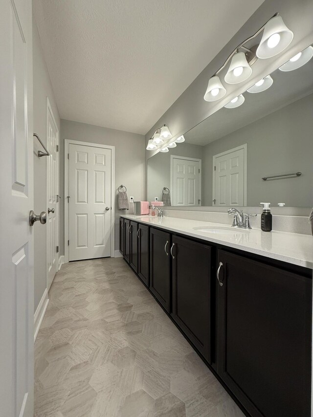 bathroom with double vanity, baseboards, a sink, and a textured ceiling