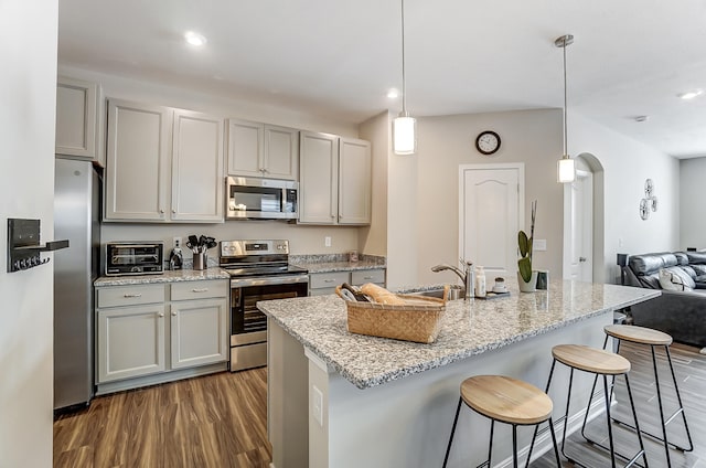 kitchen with appliances with stainless steel finishes, gray cabinetry, hanging light fixtures, light stone counters, and dark wood-type flooring