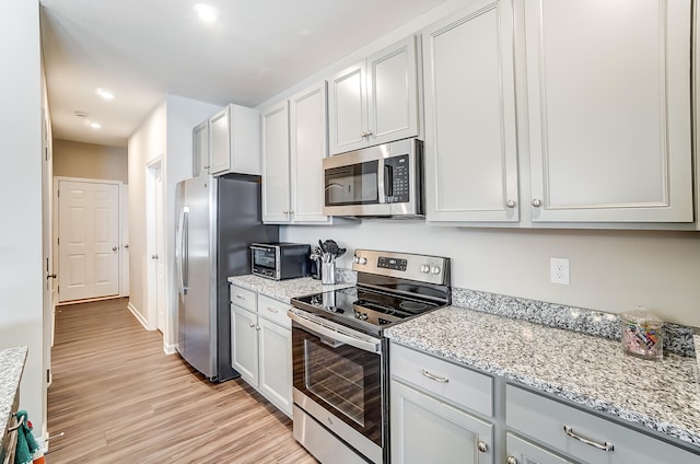 kitchen featuring light stone counters, light hardwood / wood-style flooring, stainless steel appliances, and white cabinets