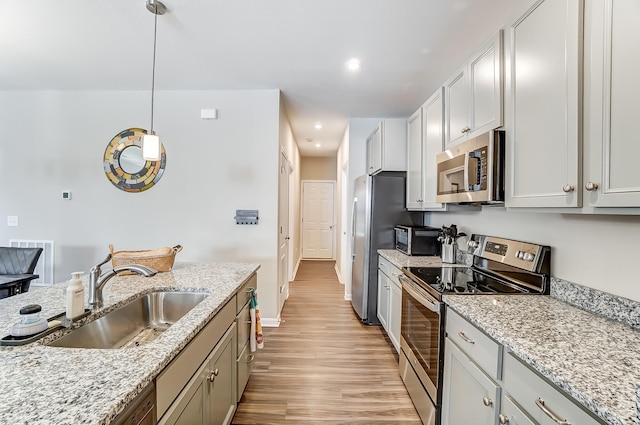 kitchen with pendant lighting, sink, light stone counters, and appliances with stainless steel finishes