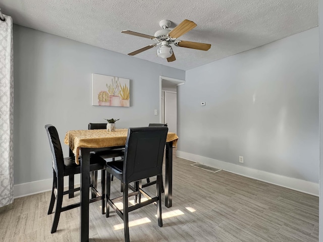 dining room with a textured ceiling, light wood-style flooring, visible vents, and baseboards