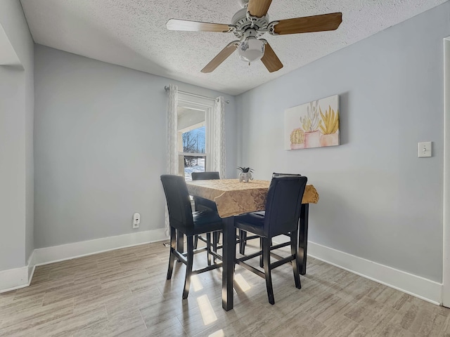 dining area featuring a textured ceiling, baseboards, and light wood-style floors