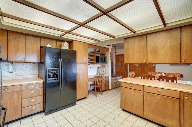 kitchen with tasteful backsplash, light countertops, light tile patterned floors, brown cabinets, and black appliances