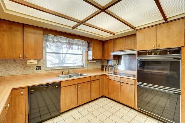 kitchen featuring brown cabinetry, a sink, black appliances, light countertops, and under cabinet range hood