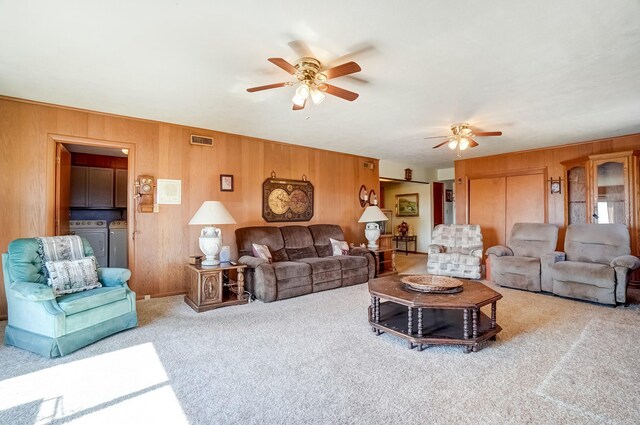 carpeted living area with wooden walls, a ceiling fan, visible vents, and washing machine and clothes dryer