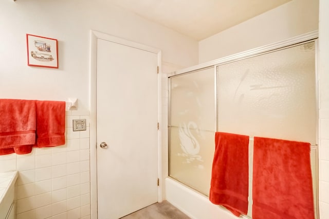 bathroom featuring combined bath / shower with glass door and tile walls