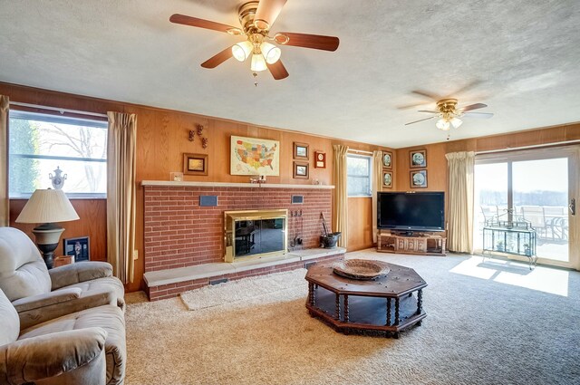 carpeted living room with wood walls, a fireplace, a textured ceiling, and ceiling fan