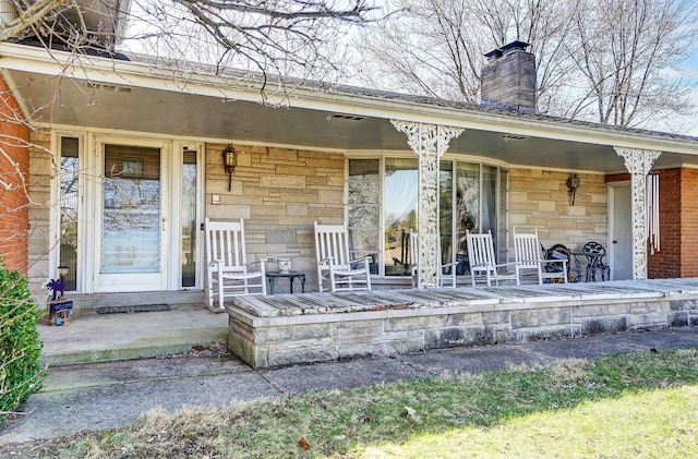 property entrance with stone siding, covered porch, and a chimney