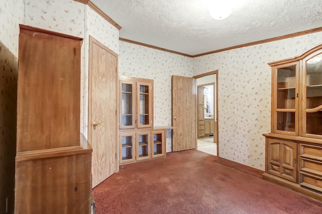 carpeted empty room featuring a textured ceiling, wallpapered walls, and crown molding