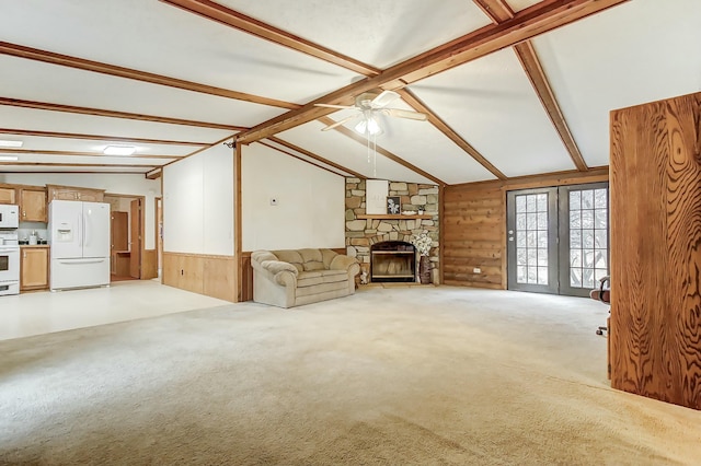 unfurnished living room featuring a ceiling fan, lofted ceiling with beams, a fireplace, wood walls, and light colored carpet