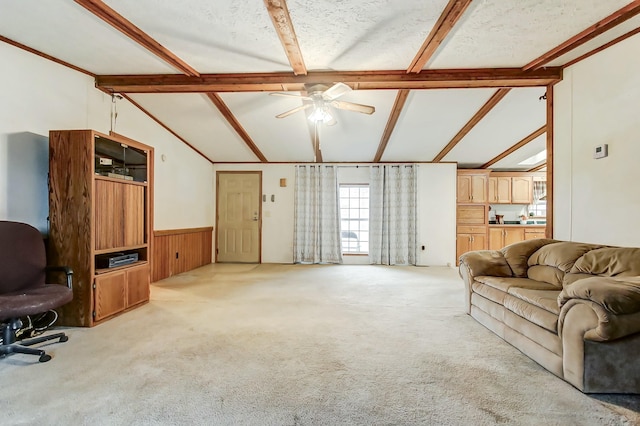 living area featuring a ceiling fan, vaulted ceiling with beams, carpet, and wainscoting