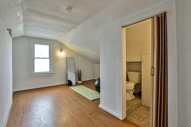 additional living space featuring lofted ceiling, a textured ceiling, baseboards, and hardwood / wood-style flooring