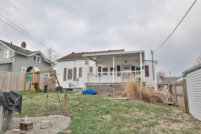 rear view of property featuring a fenced backyard, a wooden deck, a playground, and a yard