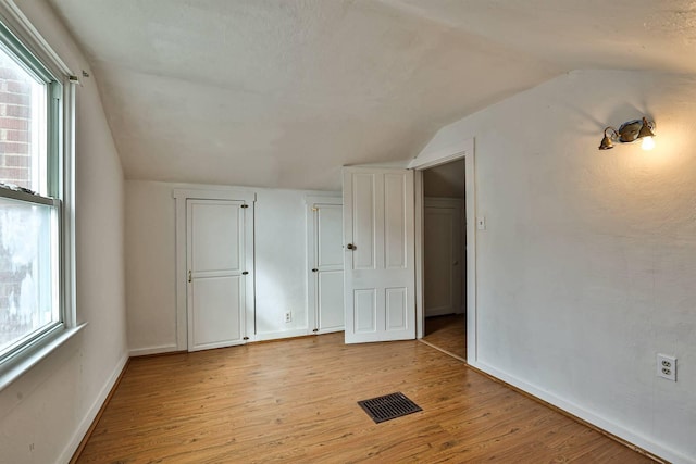 additional living space with vaulted ceiling, a wealth of natural light, light wood-type flooring, and visible vents