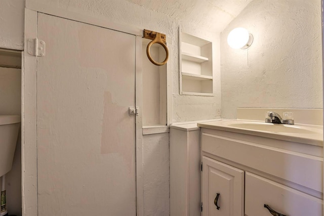 bathroom featuring built in shelves, a textured wall, vanity, and a textured ceiling