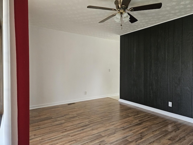 unfurnished room featuring ceiling fan, wooden walls, hardwood / wood-style floors, and a textured ceiling