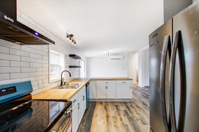 kitchen with wood counters, appliances with stainless steel finishes, under cabinet range hood, a sink, and a wall mounted AC