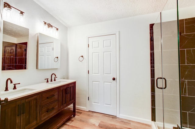 full bath with a sink, a textured ceiling, a shower stall, and wood finished floors