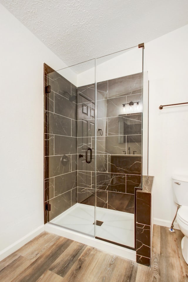 full bathroom with a textured ceiling, toilet, wood finished floors, baseboards, and a shower stall