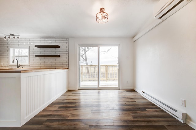 unfurnished dining area featuring dark wood-style flooring, a wall unit AC, a sink, and baseboard heating