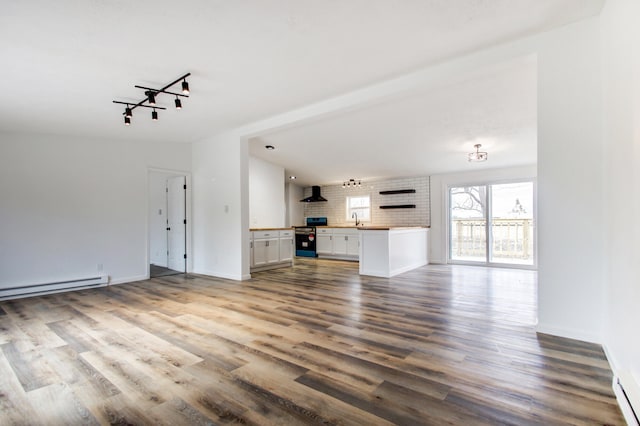 unfurnished living room with track lighting, baseboards, a baseboard radiator, wood finished floors, and a sink