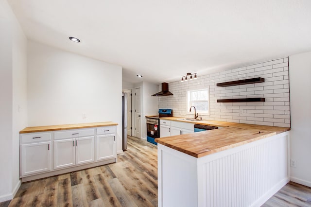 kitchen with stainless steel electric stove, decorative backsplash, a sink, wood counters, and wall chimney exhaust hood