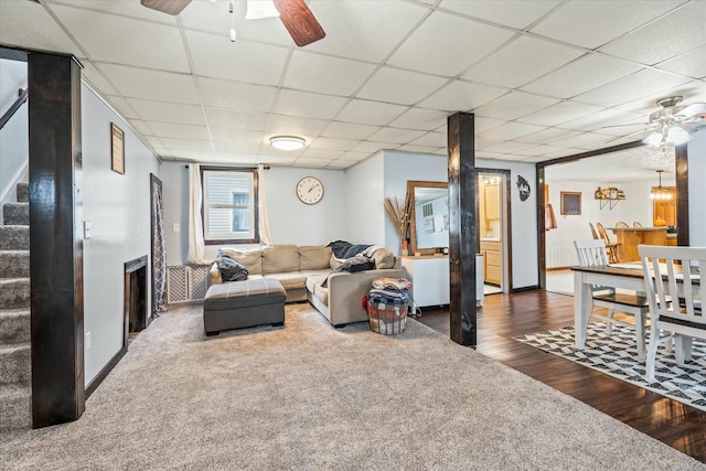 carpeted living room featuring wood finished floors, stairway, a ceiling fan, and a drop ceiling