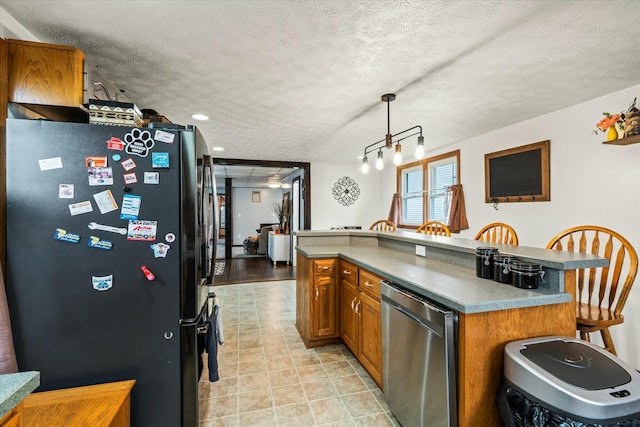 kitchen featuring a textured ceiling, brown cabinetry, freestanding refrigerator, pendant lighting, and fridge