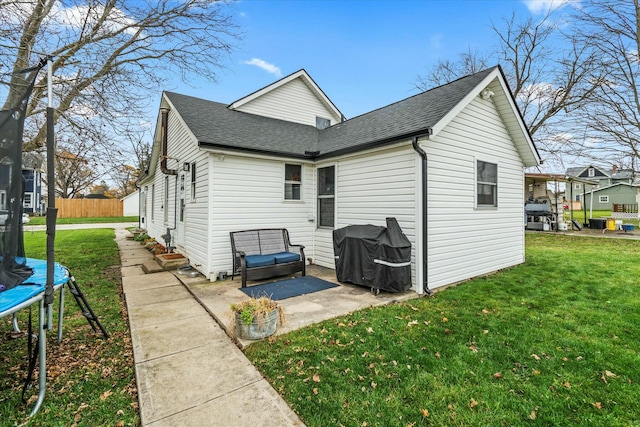 rear view of property featuring a patio, a trampoline, roof with shingles, and a lawn