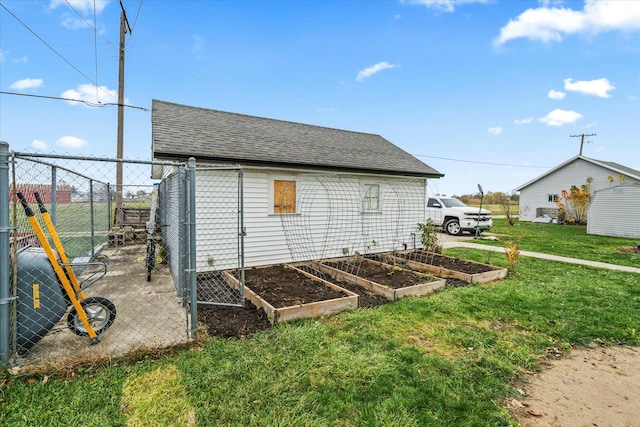 view of side of home with a garden, a yard, roof with shingles, and fence