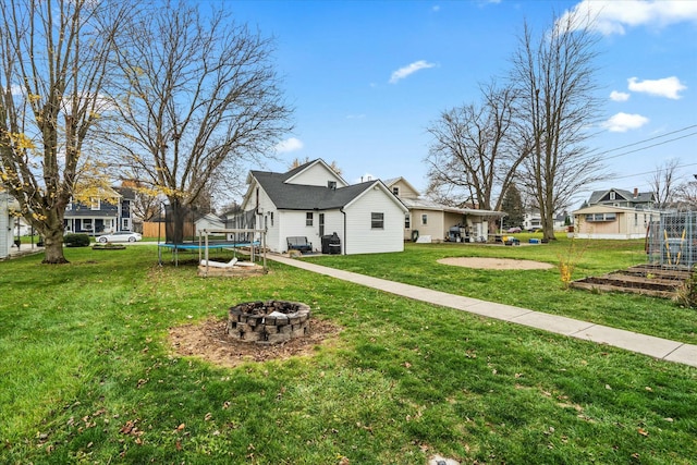 back of property with a trampoline, a fire pit, and a lawn