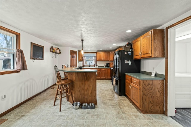 kitchen featuring a breakfast bar area, baseboards, freestanding refrigerator, a textured ceiling, and brown cabinets