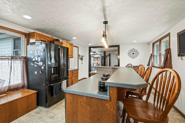 kitchen with black fridge with ice dispenser, a healthy amount of sunlight, brown cabinetry, and a textured ceiling