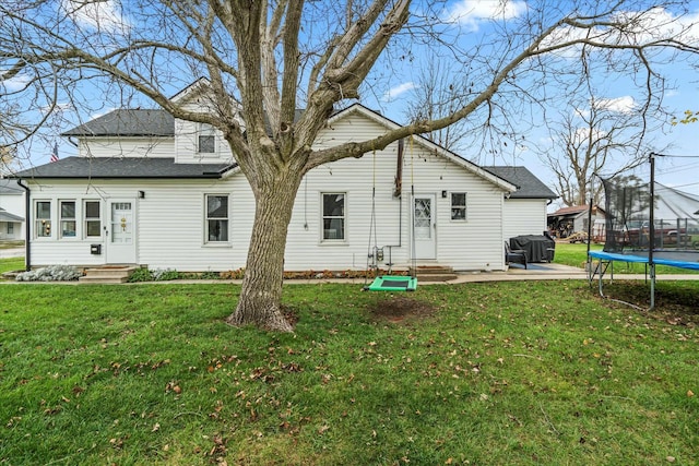 rear view of property featuring a patio, a shingled roof, entry steps, a trampoline, and a lawn