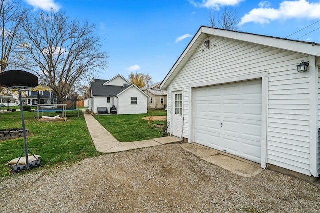 exterior space featuring an outbuilding, dirt driveway, a detached garage, a trampoline, and a lawn