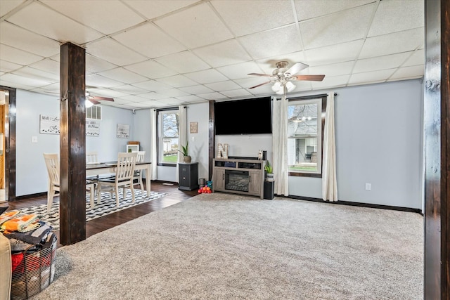 unfurnished living room with carpet, baseboards, a drop ceiling, and ceiling fan