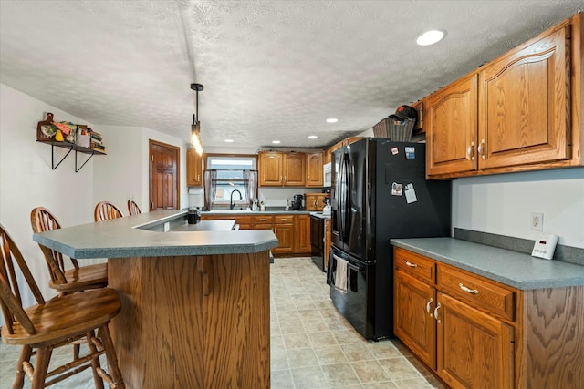 kitchen with brown cabinets, black appliances, a sink, a textured ceiling, and a breakfast bar area