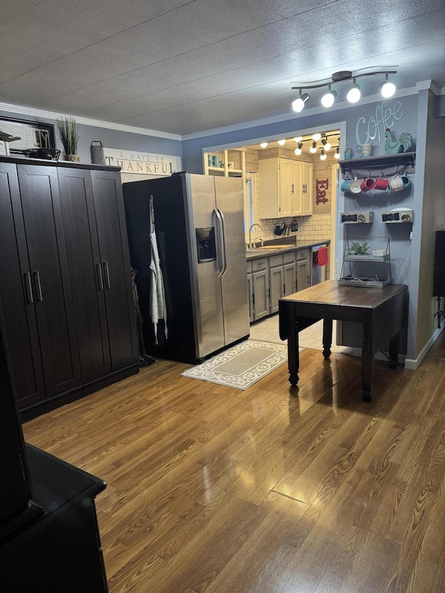 kitchen with dark cabinets, light wood-type flooring, backsplash, stainless steel fridge, and crown molding