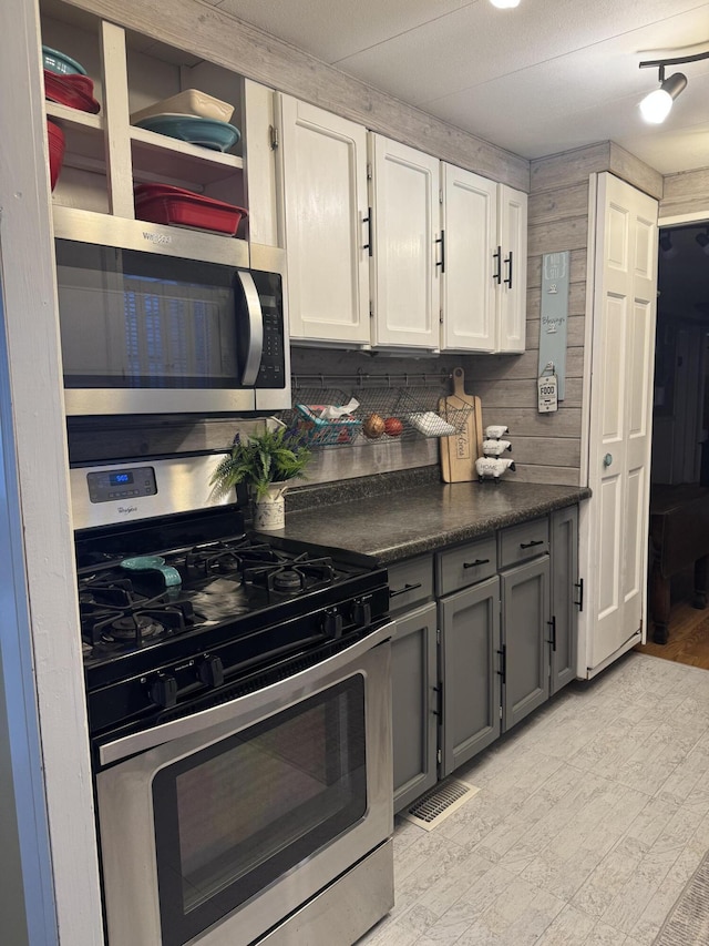 kitchen featuring wooden walls, stainless steel appliances, visible vents, gray cabinets, and dark countertops