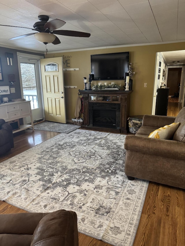 living area with ceiling fan, a fireplace, crown molding, and wood finished floors