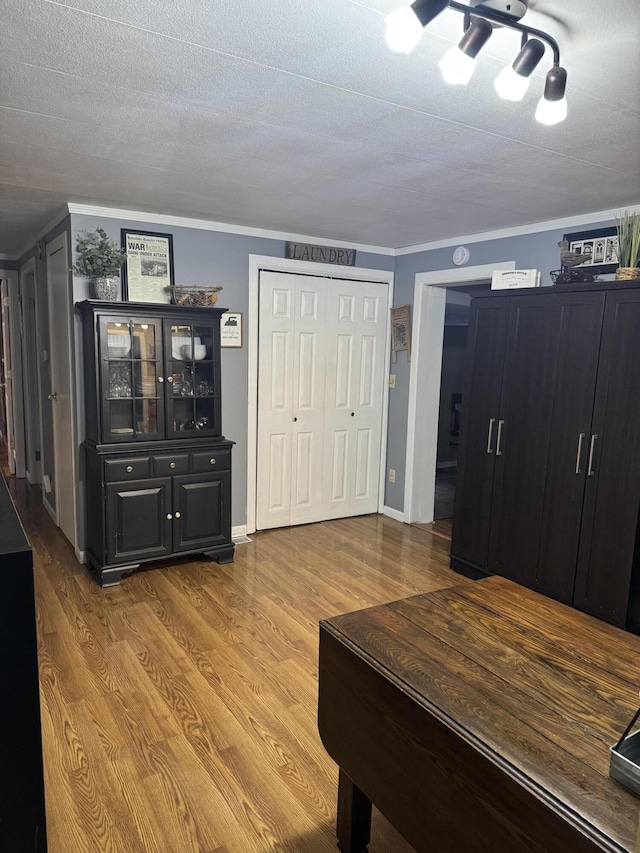 interior space featuring baseboards, a textured ceiling, ornamental molding, and wood finished floors