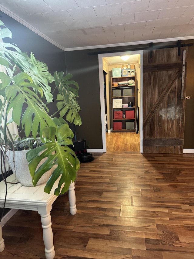 hall featuring ornamental molding, a barn door, baseboards, and wood finished floors