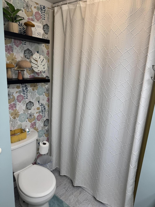 bathroom with curtained shower, toilet, and wallpapered walls