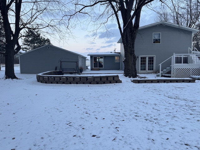 snow covered property featuring a garage, an outbuilding, and a wooden deck