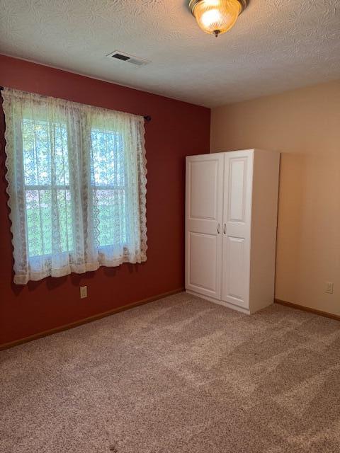 unfurnished bedroom featuring light colored carpet, baseboards, a textured ceiling, and visible vents