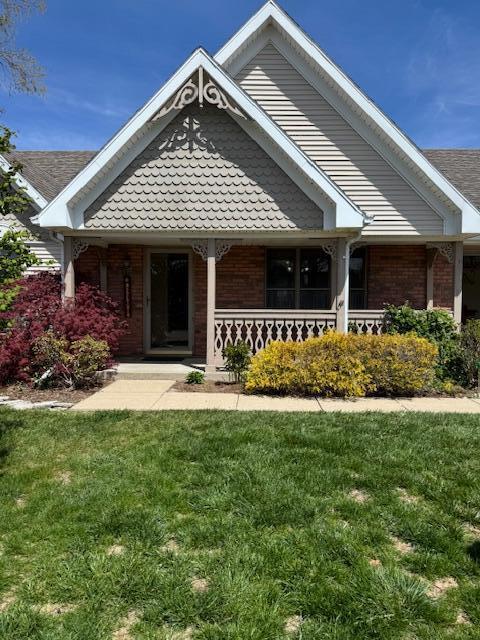 craftsman house with a porch, a front lawn, and brick siding