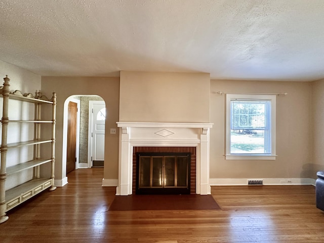 unfurnished living room featuring a baseboard heating unit, a brick fireplace, dark hardwood / wood-style floors, and a textured ceiling