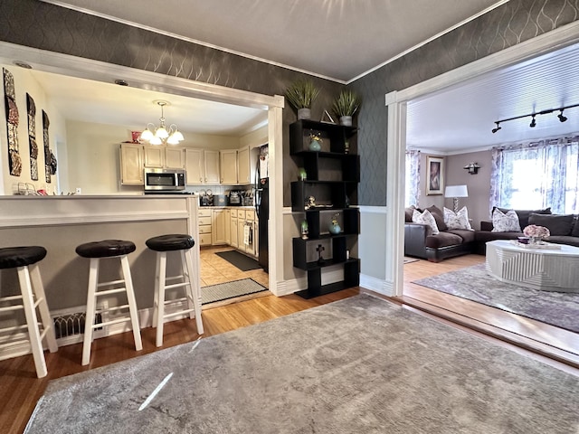 kitchen with a kitchen bar, crown molding, decorative light fixtures, a chandelier, and light hardwood / wood-style floors