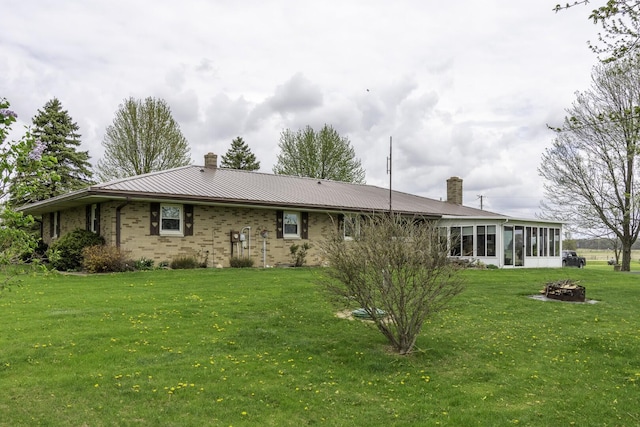 back of house with a sunroom, a chimney, a lawn, brick siding, and a fire pit